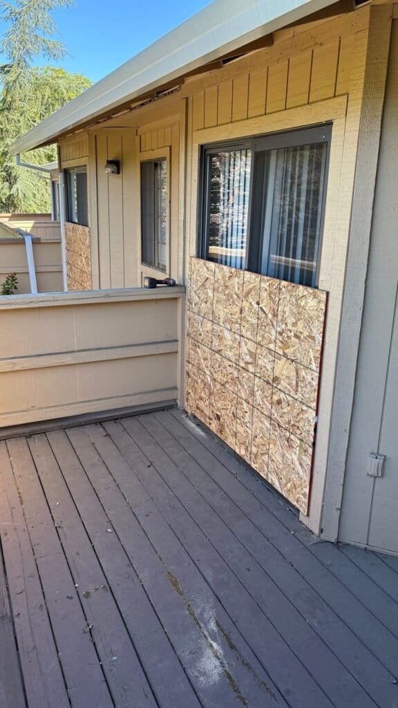 Worn painted deck boards and temporary sheathing on a townhome balcony before replacement
