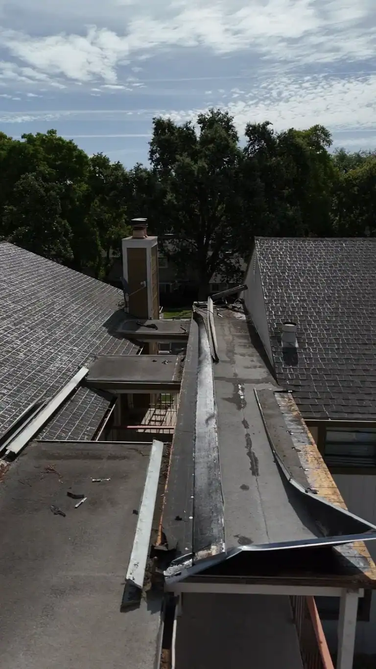 Close aerial view of patched low-slope roofing and detached edge metal above an apartment walkway