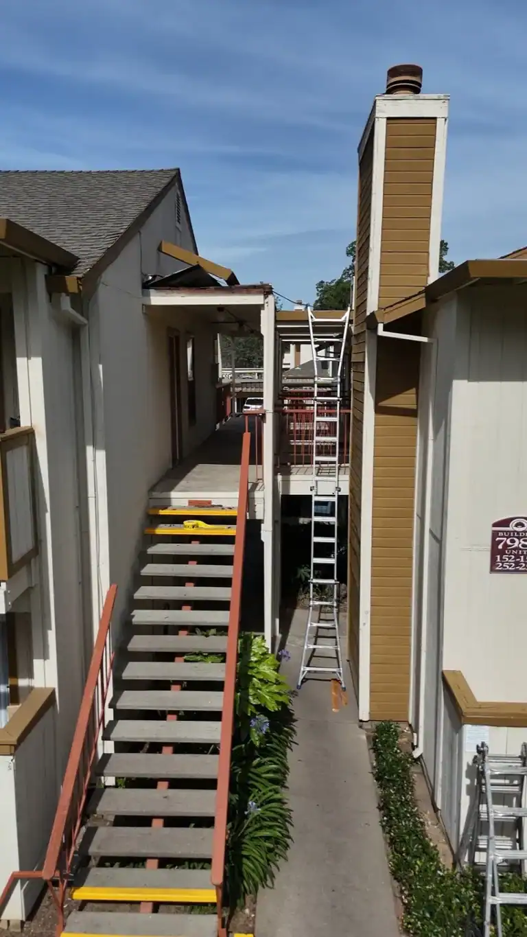 Ladders staged at the exterior stairs during walkway and roof work at a Citrus Heights apartment community