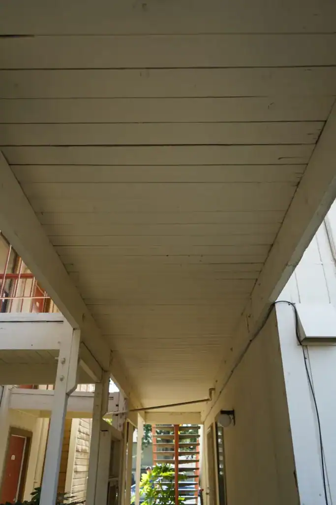 Water-stained soffit boards and peeling paint on the beams above an apartment walkway