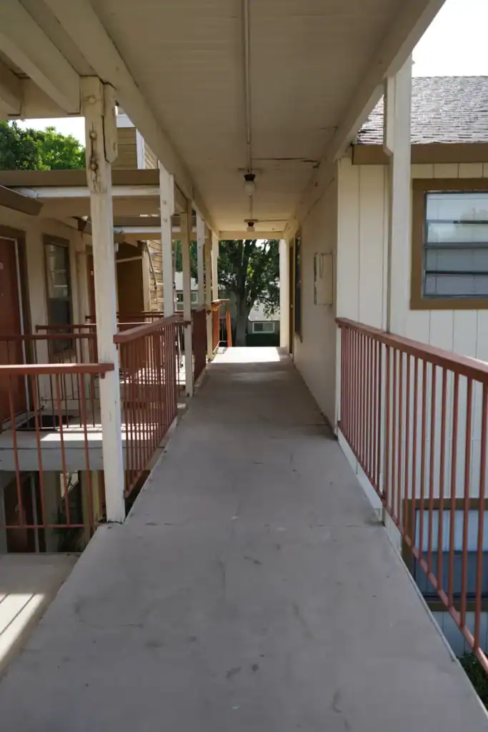 Worn bare concrete walkway with weathered posts and stained ceiling before waterproofing