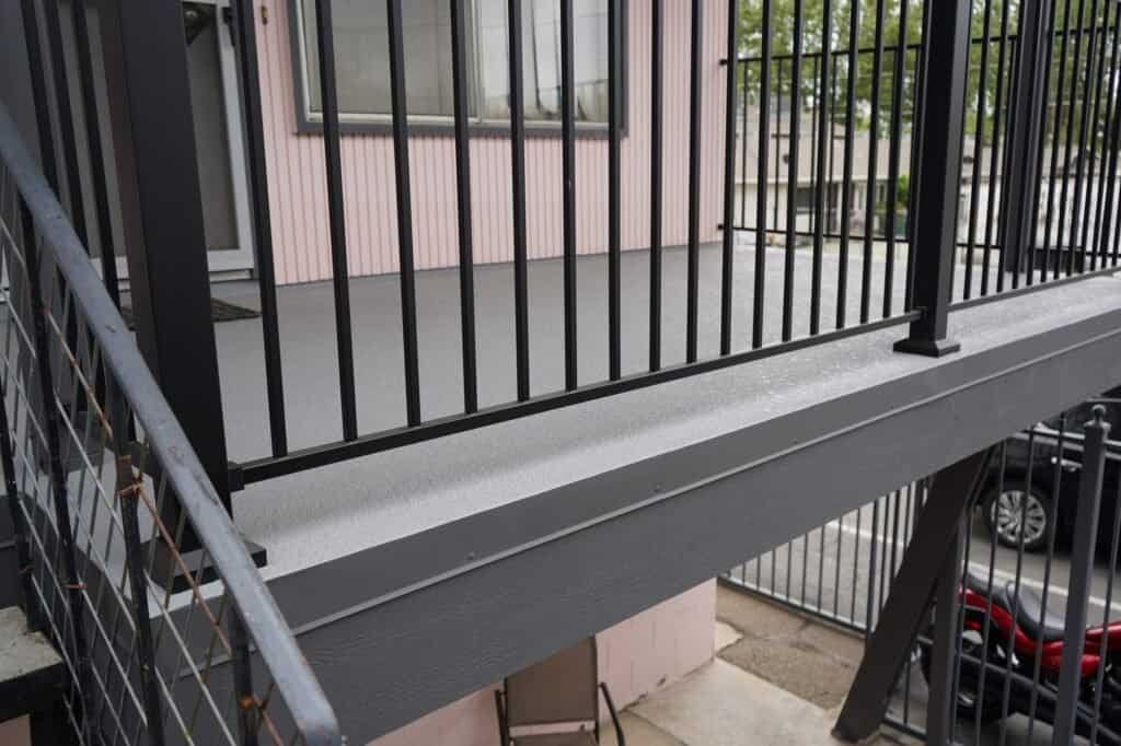 Same apartment walkway after replacement, with new waterproof deck coating, fascia and aluminum railing