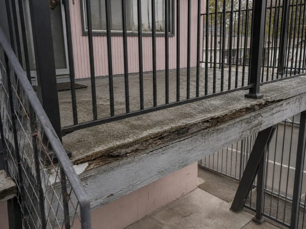 Dry-rotted rim joist and failed deck coating on an apartment walkway before repair in Lodi, California