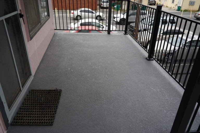 Private apartment balcony with new waterproof coating and black aluminum railing overlooking the parking lot