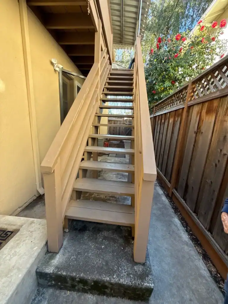 Old wood apartment stairway with a flat board handrail and weathered treads before replacement