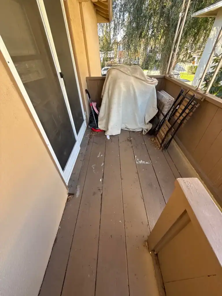 Split and stained painted deck boards on an apartment balcony before composite replacement