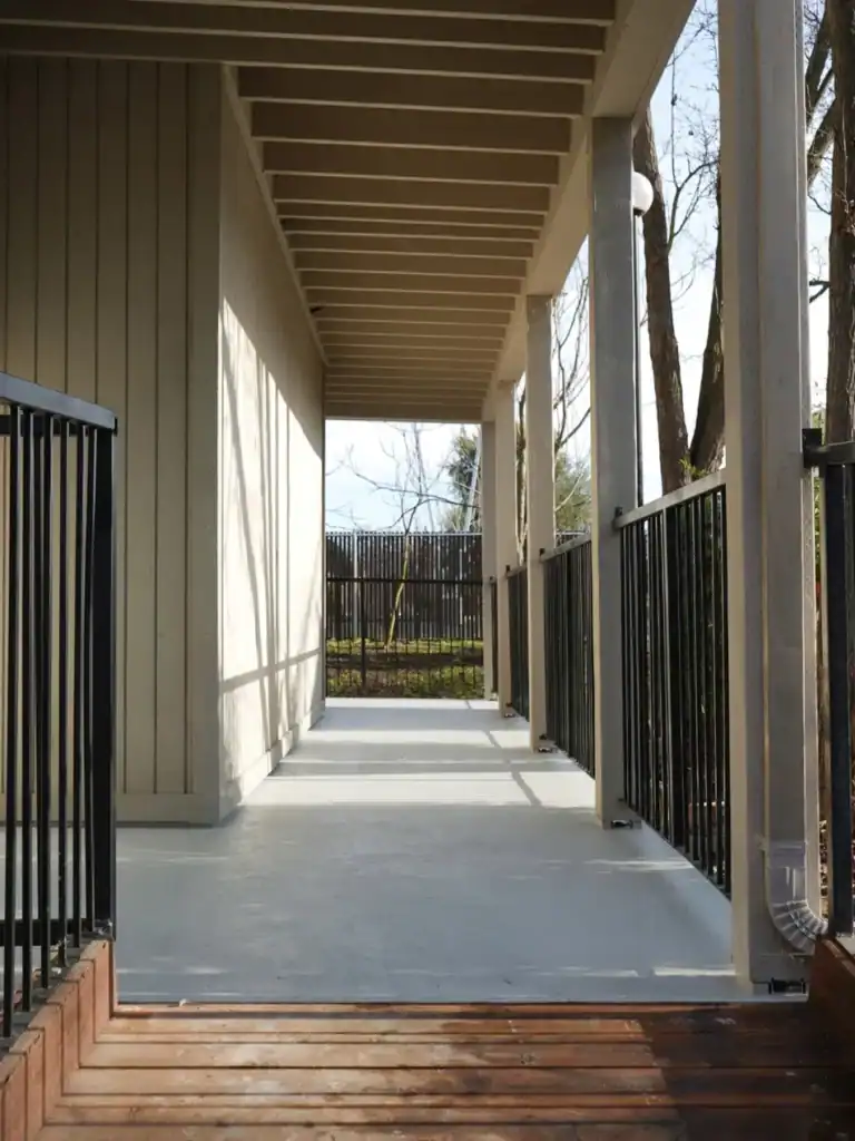 Elevated apartment walkway after waterproofing, with new gray deck coating and repainted structure