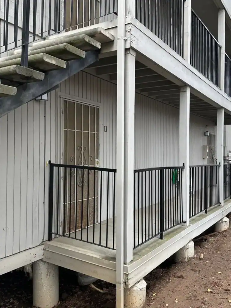 Two-story apartment building with weathered elevated walkway and deck structure before repair