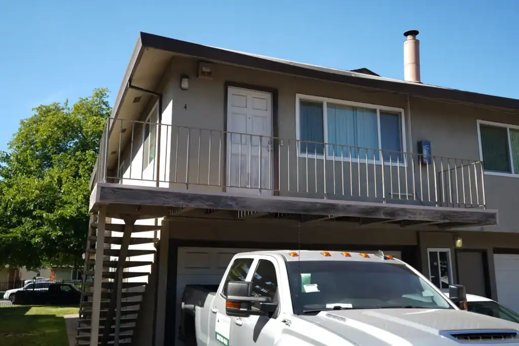 Entry balcony over a garage in Sacramento with weathered board decking and an old metal railing before reconstruction