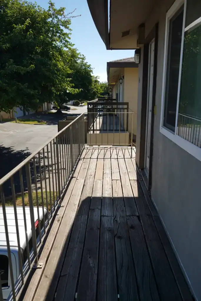 Grey splintered deck boards along an apartment entry balcony before the work