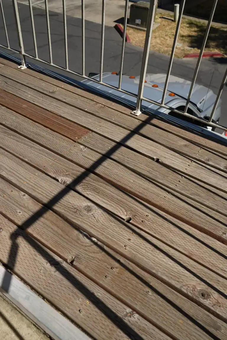 Close view of split deck boards, open gaps and rusting railing base plates before removal