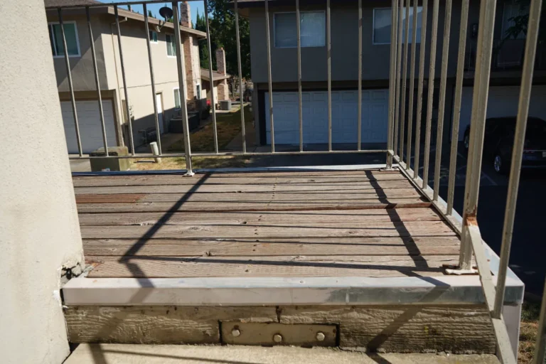 Worn balcony decking with open gaps and an old metal railing overlooking the garages before removal