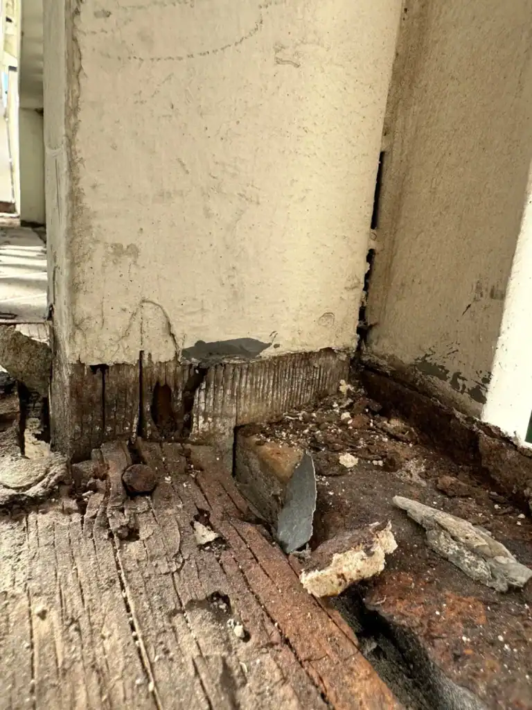 Dry-rotted framing and rusted fasteners uncovered where the balcony deck meets the stucco wall