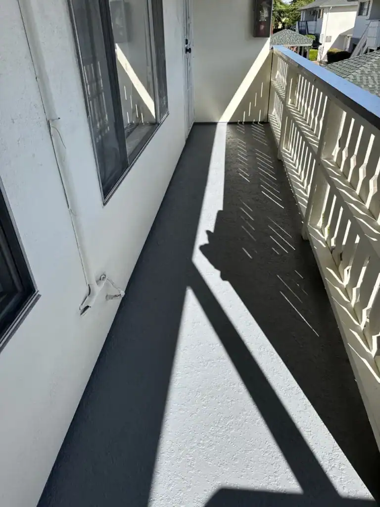 Finished apartment balcony with a dark grey textured waterproof deck coating turned up at the stucco wall