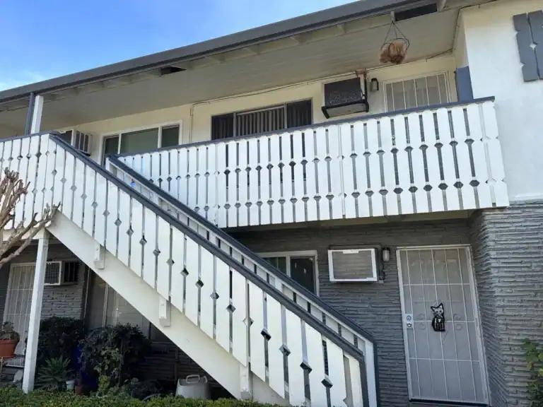 Two-story apartment building with repainted white balustrades along the balcony and stair run after repair