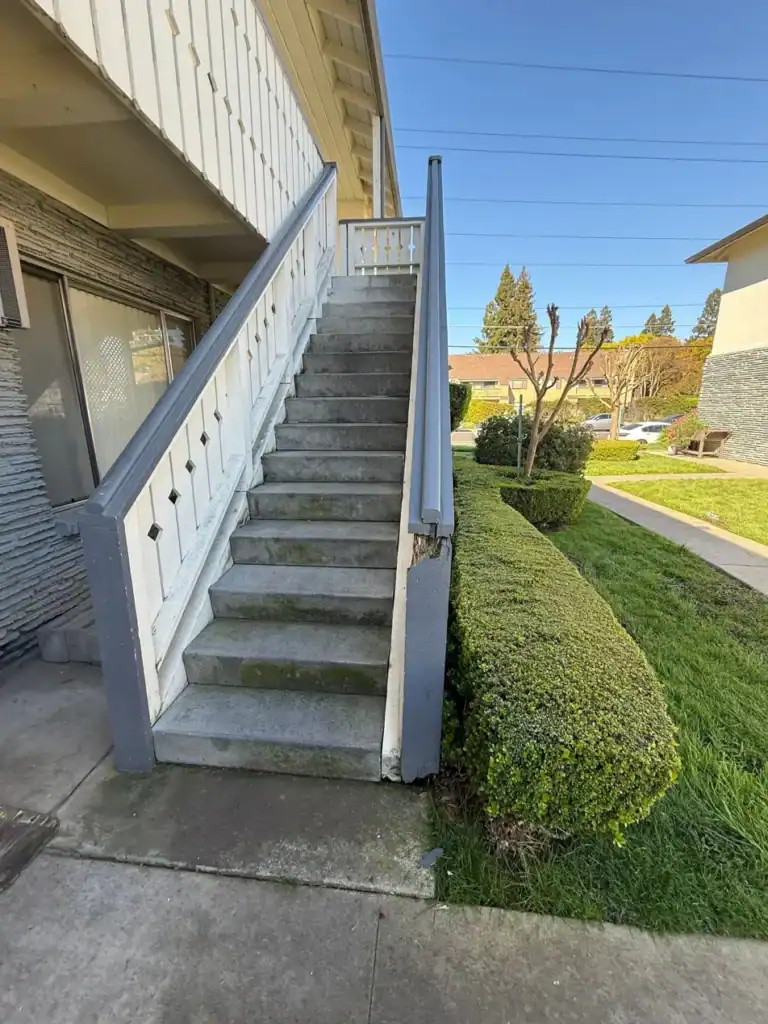 Weathered apartment stairway in Sacramento with mossy concrete treads and a split, rotted post at the base of the handrail before repair