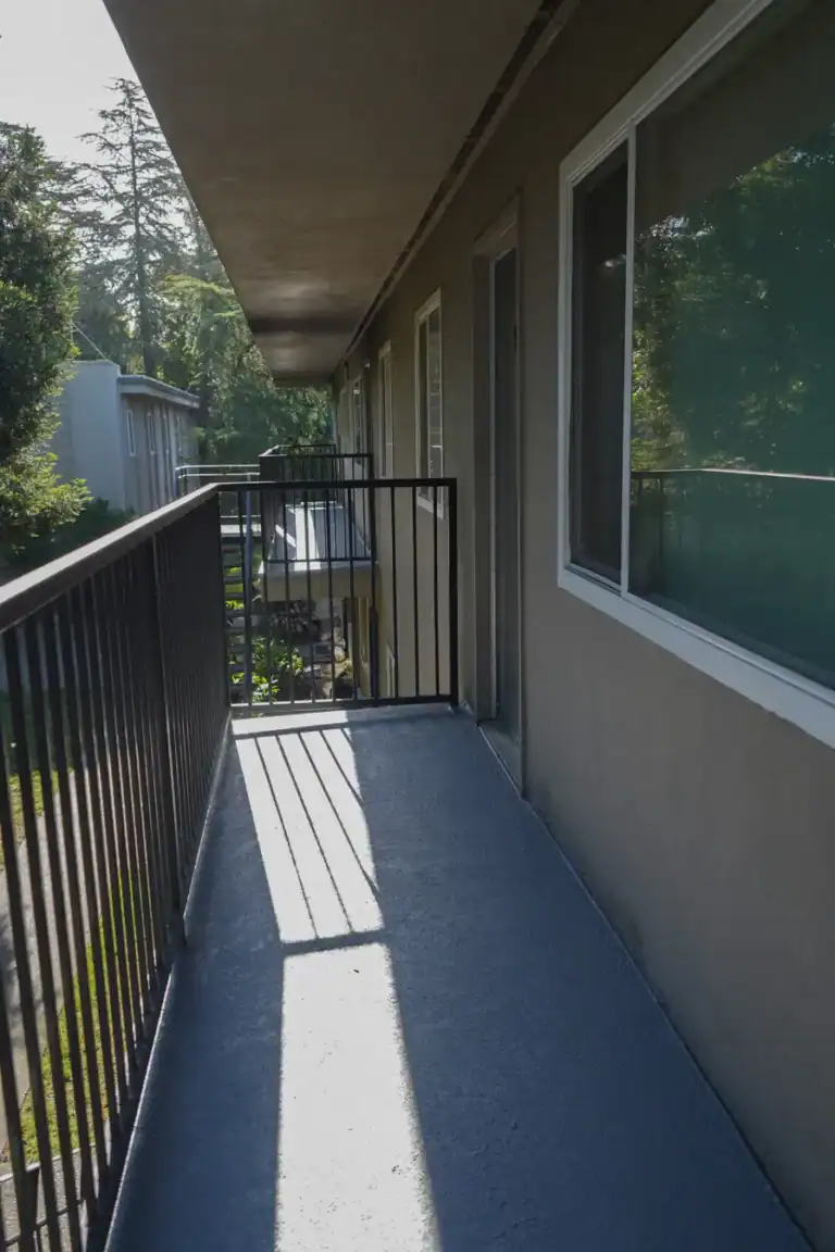 Apartment walkway in Sacramento after waterproofing, with a textured grey traffic coating carried up the wall and over the deck edge