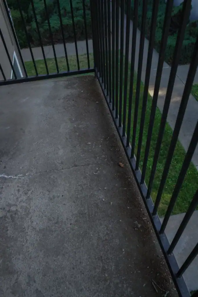 Cracked bare concrete balcony deck with efflorescence and debris packed against the railing before coating