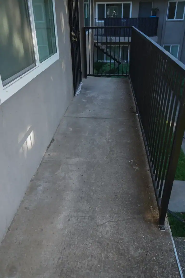 Uncoated concrete apartment walkway with a towel laid along a unit door threshold before the work