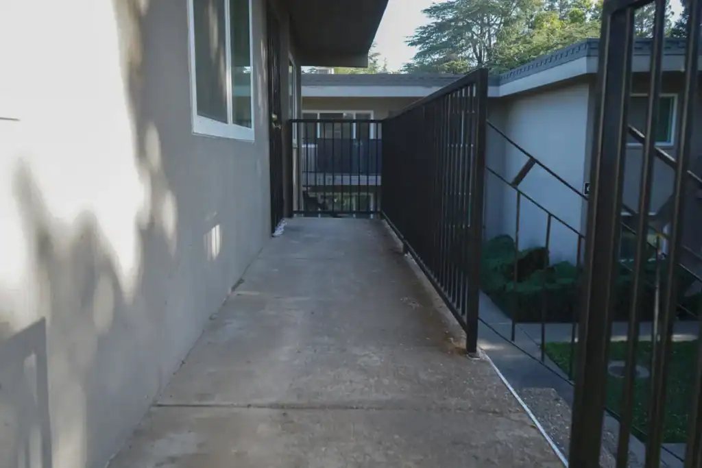 Uncoated concrete apartment walkway in Sacramento with worn slab and steel guardrail before waterproofing