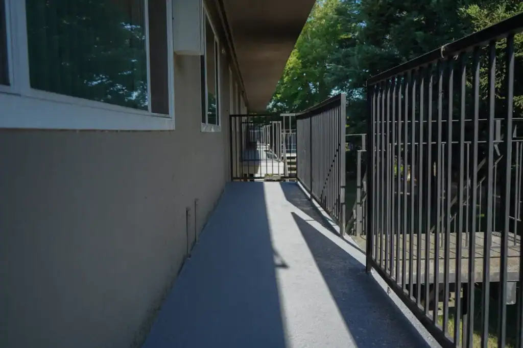 The same walkway after waterproofing, with a textured grey membrane coved up the wall and carried to the edge