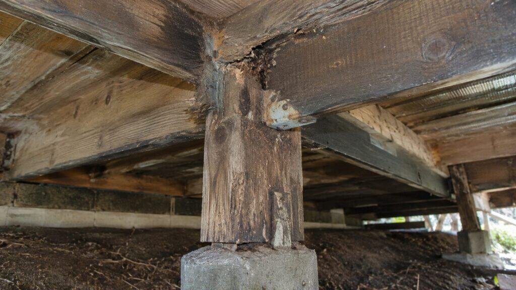 Rotted post-to-beam connection with a corroded bracket under a coastal deck before repair in Daly City