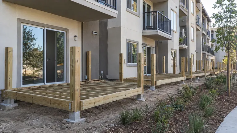 Local deck installation services — deck framing installed in sequence along a row of ground-floor apartment patios