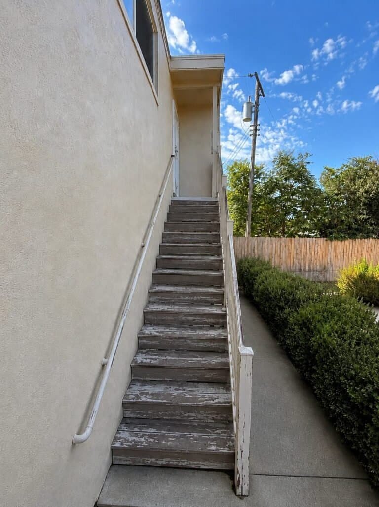 Weathered painted wood apartment stair in Elk Grove with flaking treads and a rotting newel post before replacement