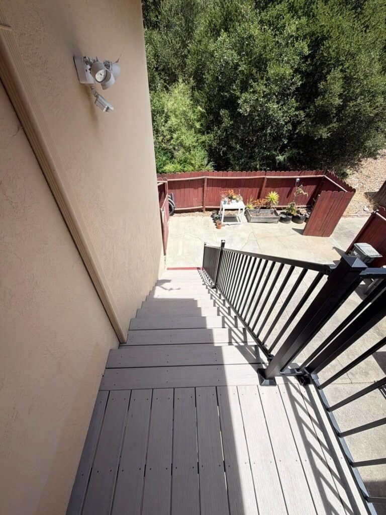 Looking down the rebuilt Oakland apartment stair from the landing, composite treads and aluminum guard