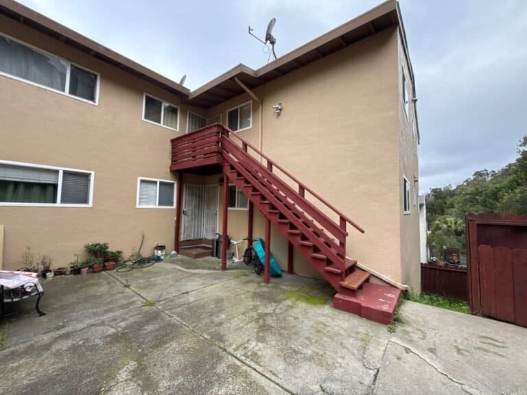 Two-story Oakland apartment building with a painted wood exterior stair and slatted balcony landing before replacement