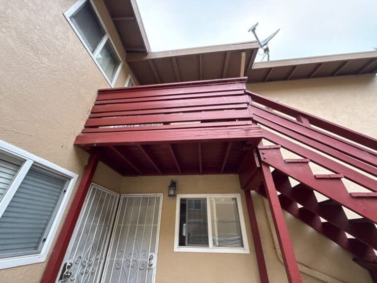 Underside of an Oakland apartment balcony landing, open wood joists and gapped deck boards above a unit entry