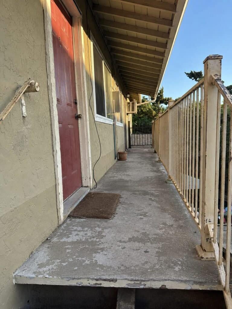 Worn cement topping and weathered wood guardrail on a San Jose apartment walkway before reconstruction