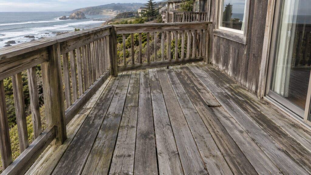 Weathered grey ocean-view deck boards and worn wood railing before replacement in San Mateo