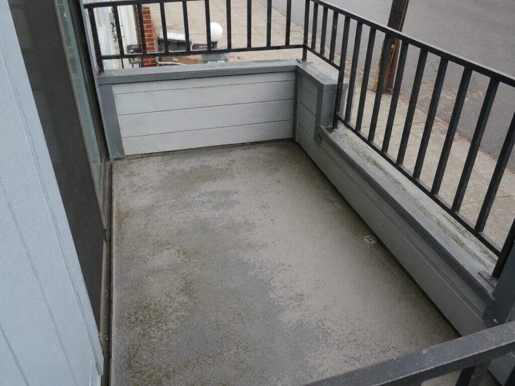 Worn and stained balcony deck coating in Vacaville with debris collected along the wall base and drain before recoating