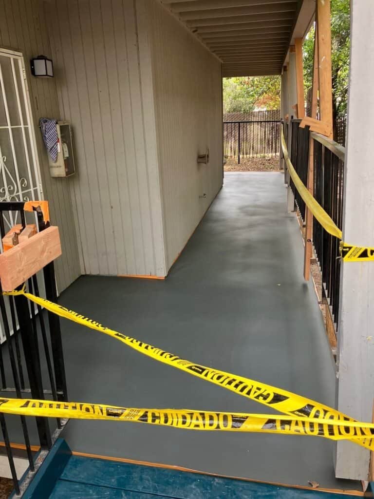 Freshly applied waterproof deck coating on a Rio Linda apartment walkway, still taped off