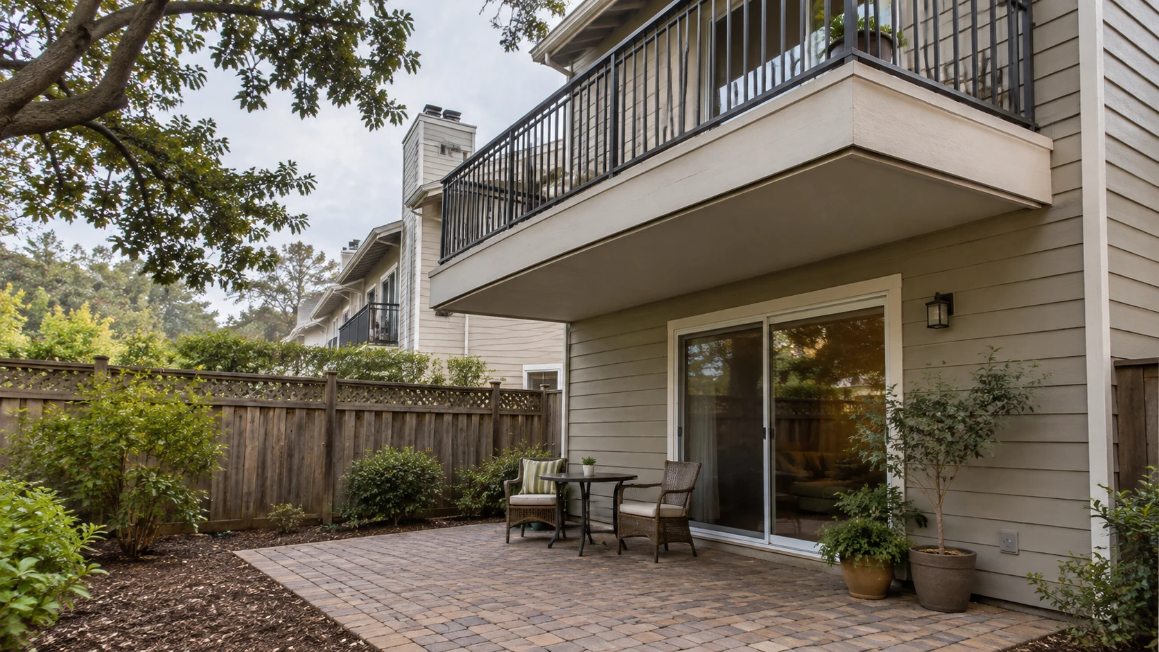 Cantilevered balcony above a brick-paver patio with a bistro set