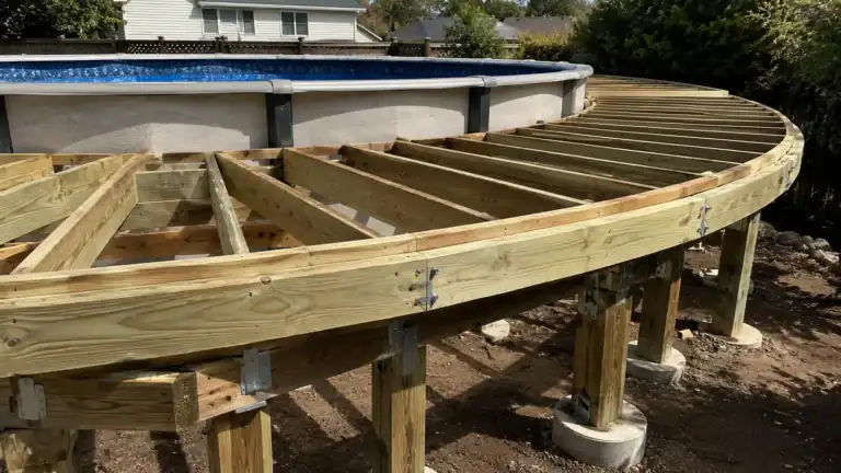 Freestanding deck frame on its own posts and footings, standing clear of an above-ground pool wall