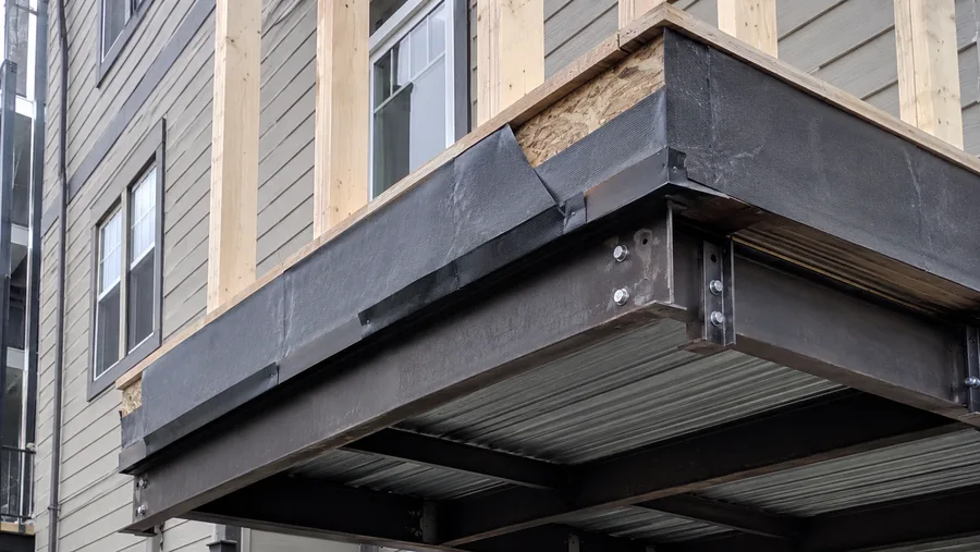 Balcony edge with membrane wrapped over the rim and steel framing beneath, mid-construction