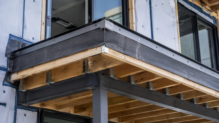 Balcony under construction with waterproofing membrane carried over the edge, edge metal, and steel and timber framing below