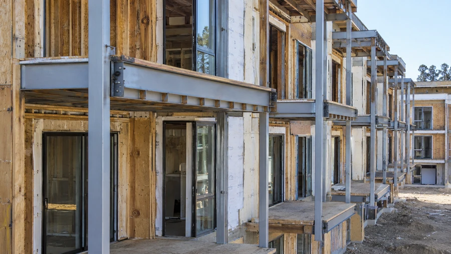 Steel-framed balconies on a multi-unit building under construction with plywood decks and sliding door openings