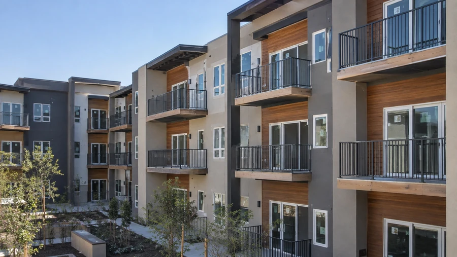 Three-story multi-unit building with black metal balcony railings above a landscaped courtyard