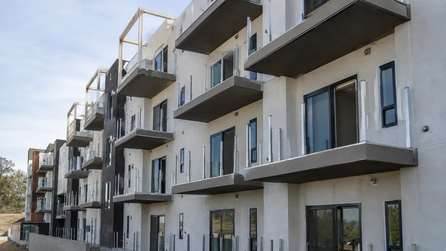 Multi-story stucco building under construction with balcony slabs and railing posts, panels not yet installed