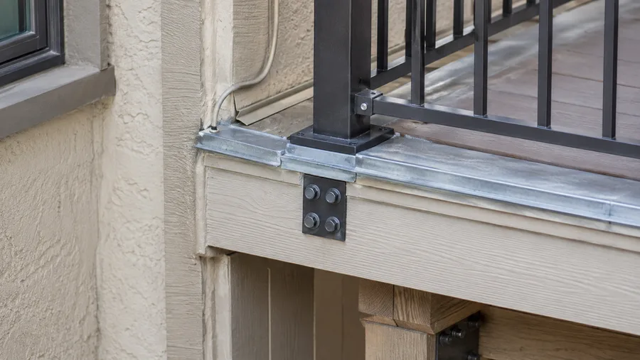 Balcony guardrail post base mounted on new edge metal, with a bolted structural bracket at the rim