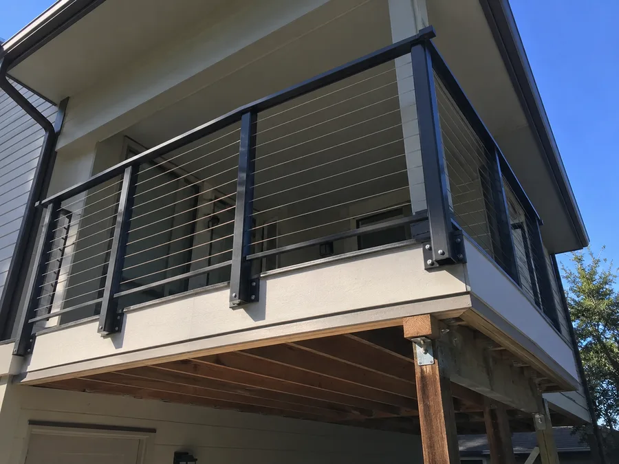 Fascia-mounted balcony railing posts bolted to the side of the structure, with cable infill