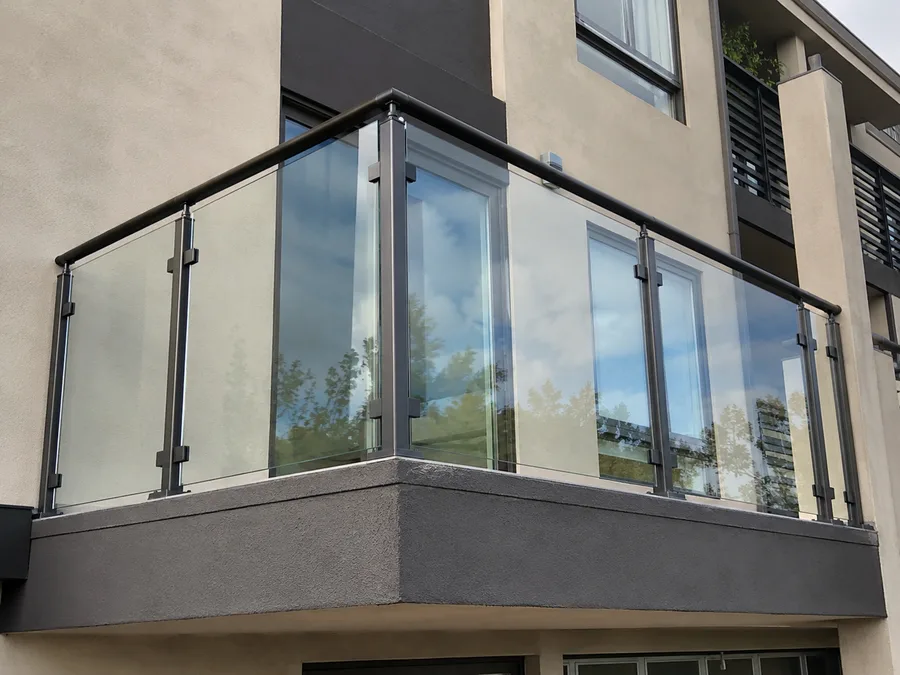 Glass panel balcony guardrail with metal posts and a rounded top rail