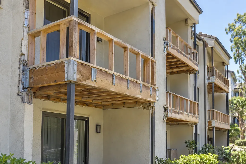 Several balconies in a row stripped to bare framing, each on a new steel post, with the stucco opened at the wall