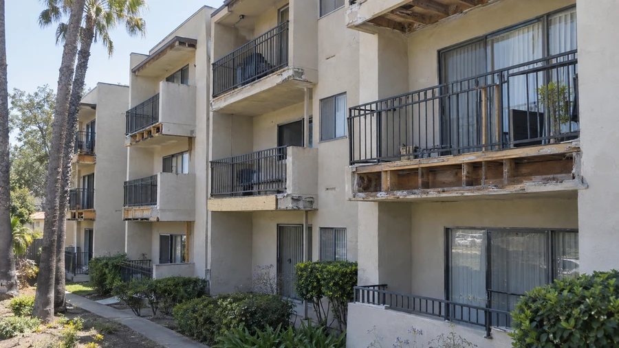 Three story stucco apartment building with balcony edges stripped to exposed wood framing