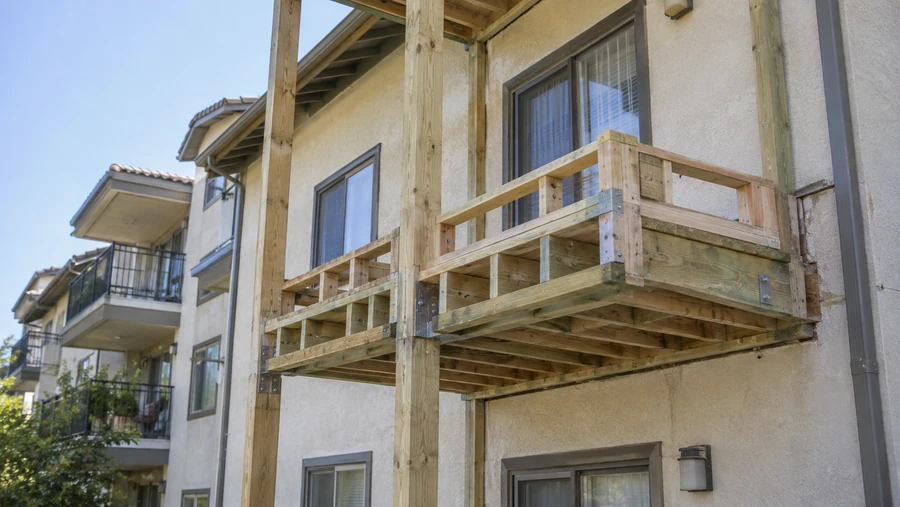 Replacement balcony framed on posts with new guardrail framing, on an occupied building