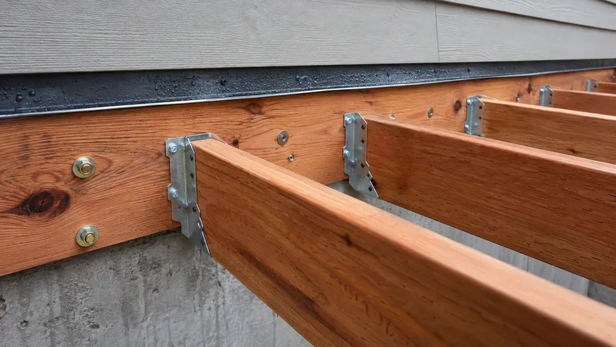 Cedar deck ledger bolted to the wall with flashing over it, joist hangers and structural bolts