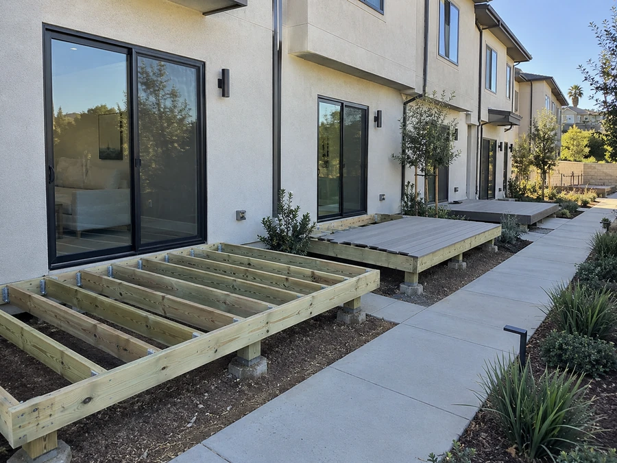 New deck framing on posts beside a completed composite deck at a townhome community